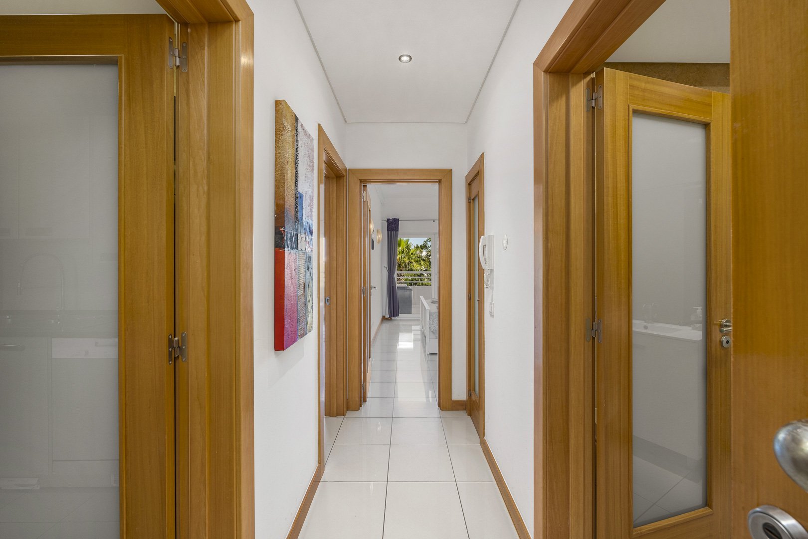 Hallway with artwork and doors leading to the bedrooms and kitchen