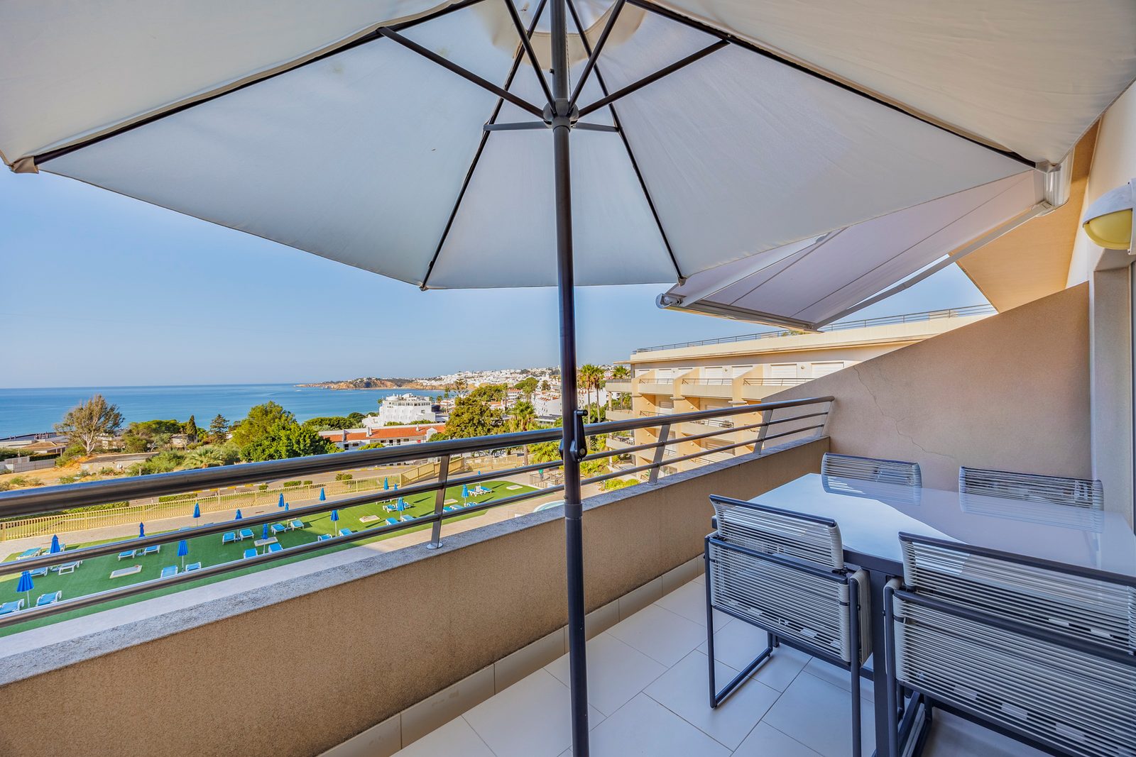 Balcony dining table under a parasol, with pool and sea view