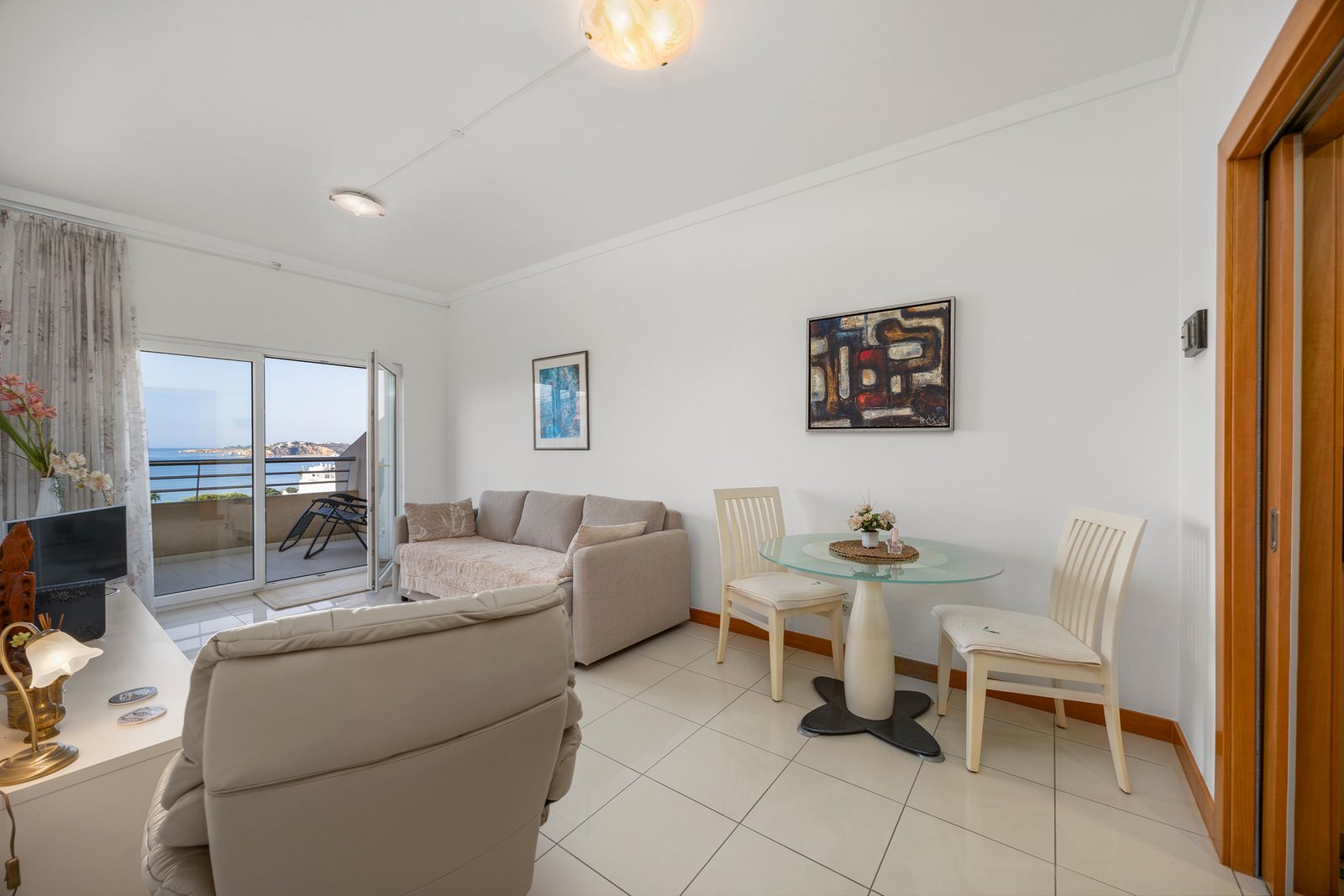 Living and dining area with sofa, glass dining table, and sea-view balcony