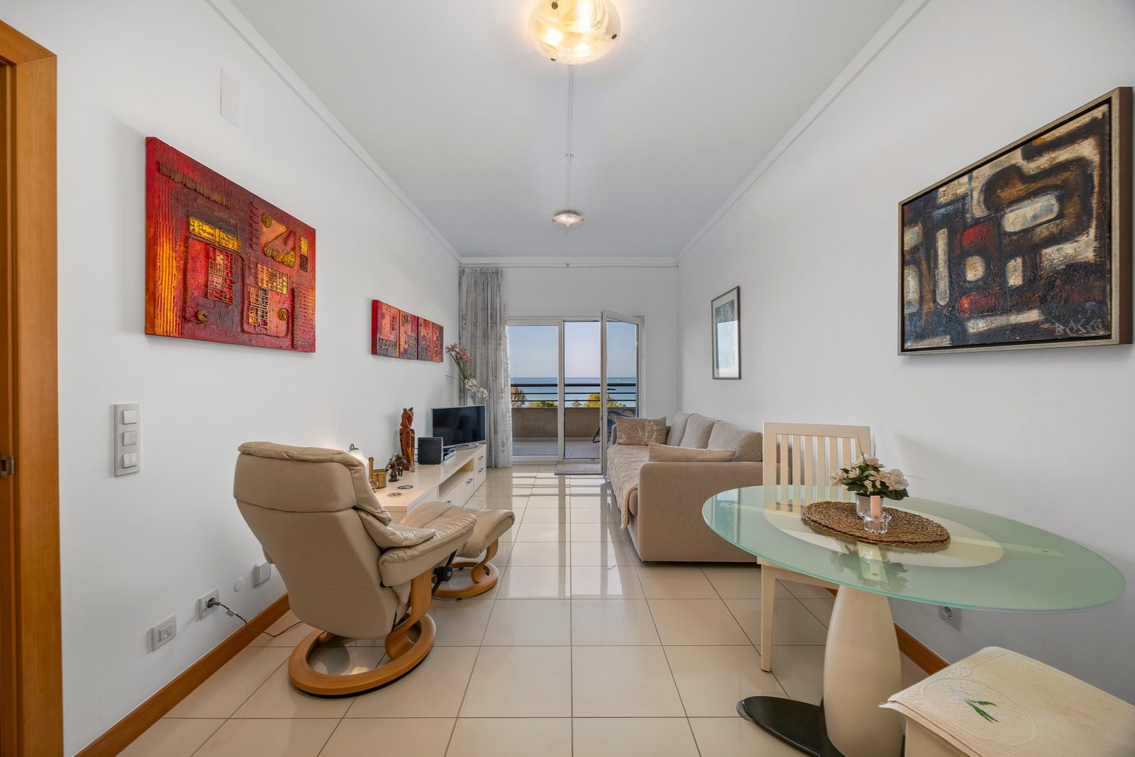 Living room with reclining armchair, glass dining table, and sea-view balcony beyond