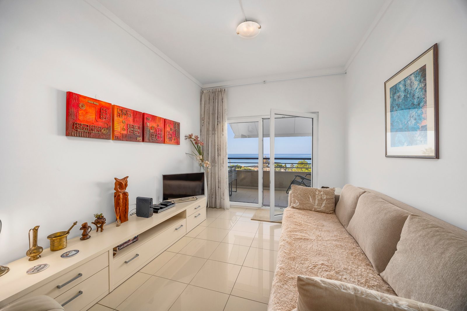 Sofa, TV unit, and open balcony doors with sea view