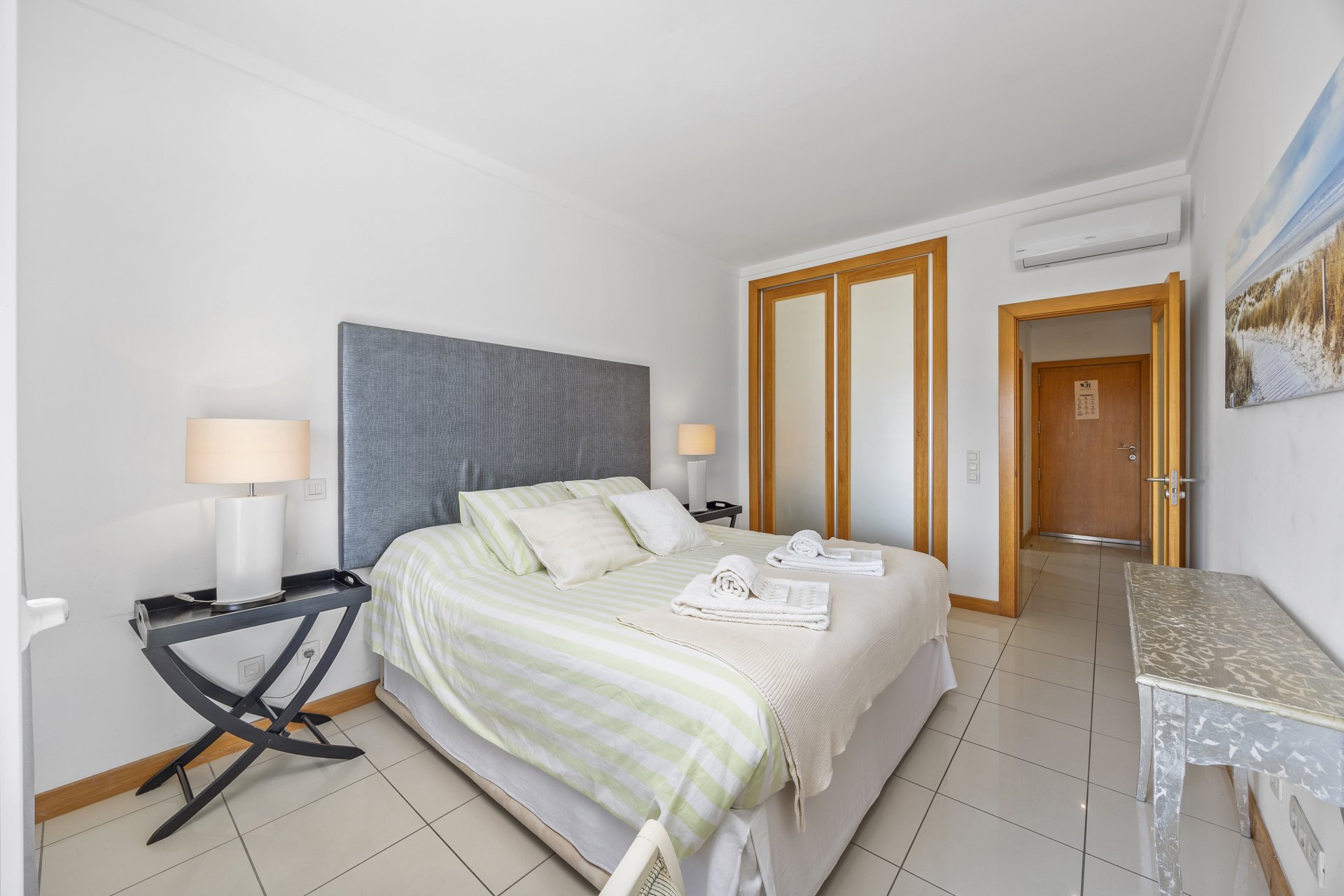 Bedroom with grey upholstered headboard, wardrobe, and hallway access