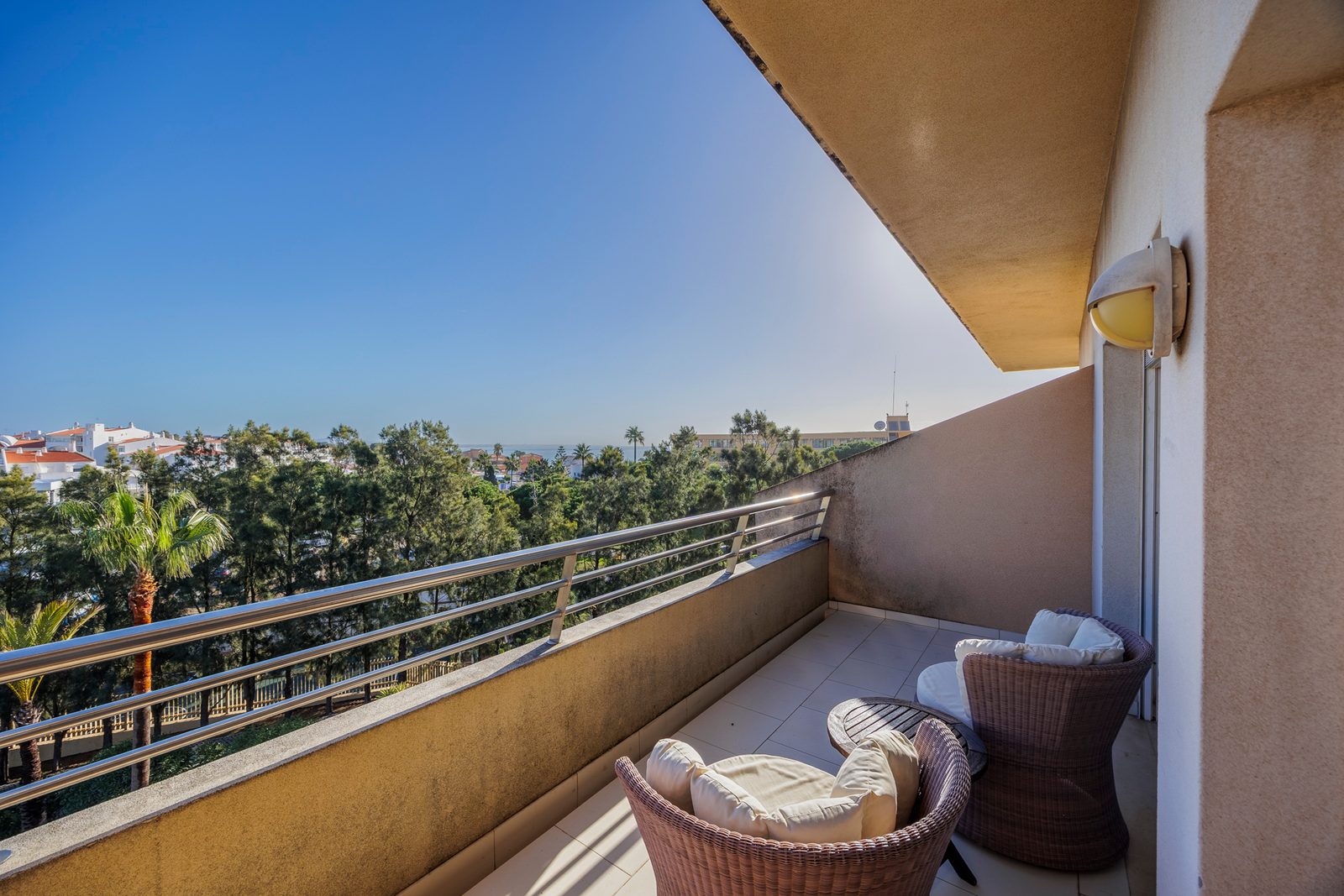 Balcony with wicker armchairs and a view over pine trees and palms