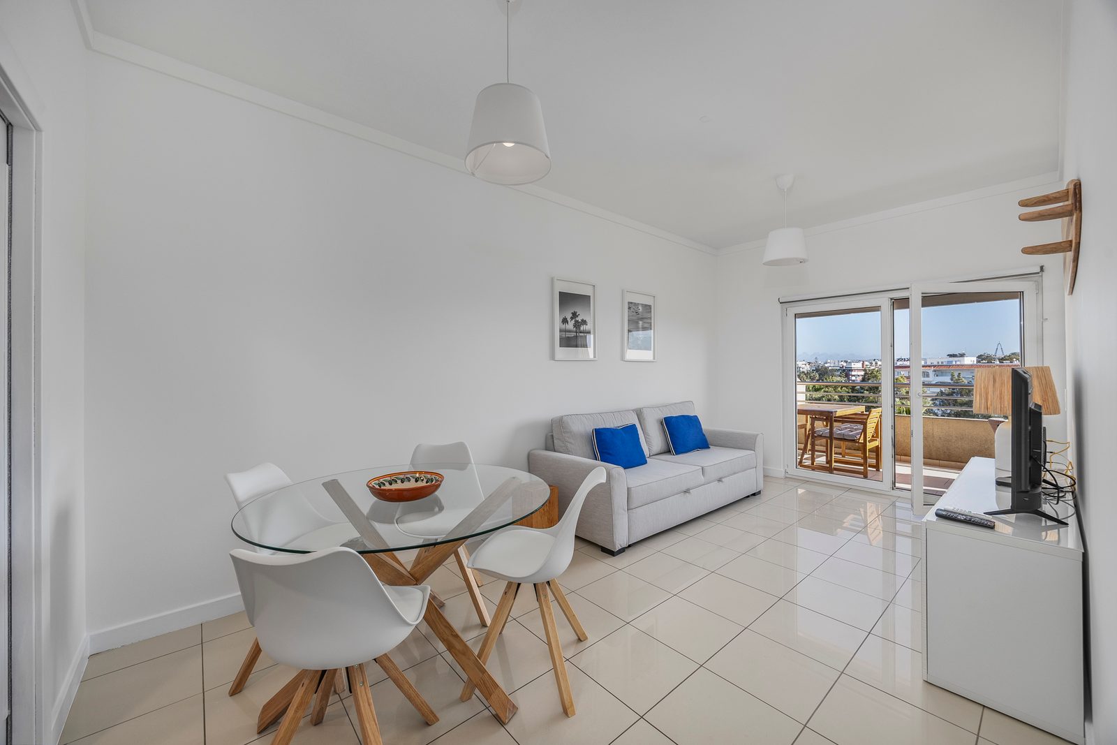 Living room with glass dining table, sofa bed, and balcony access