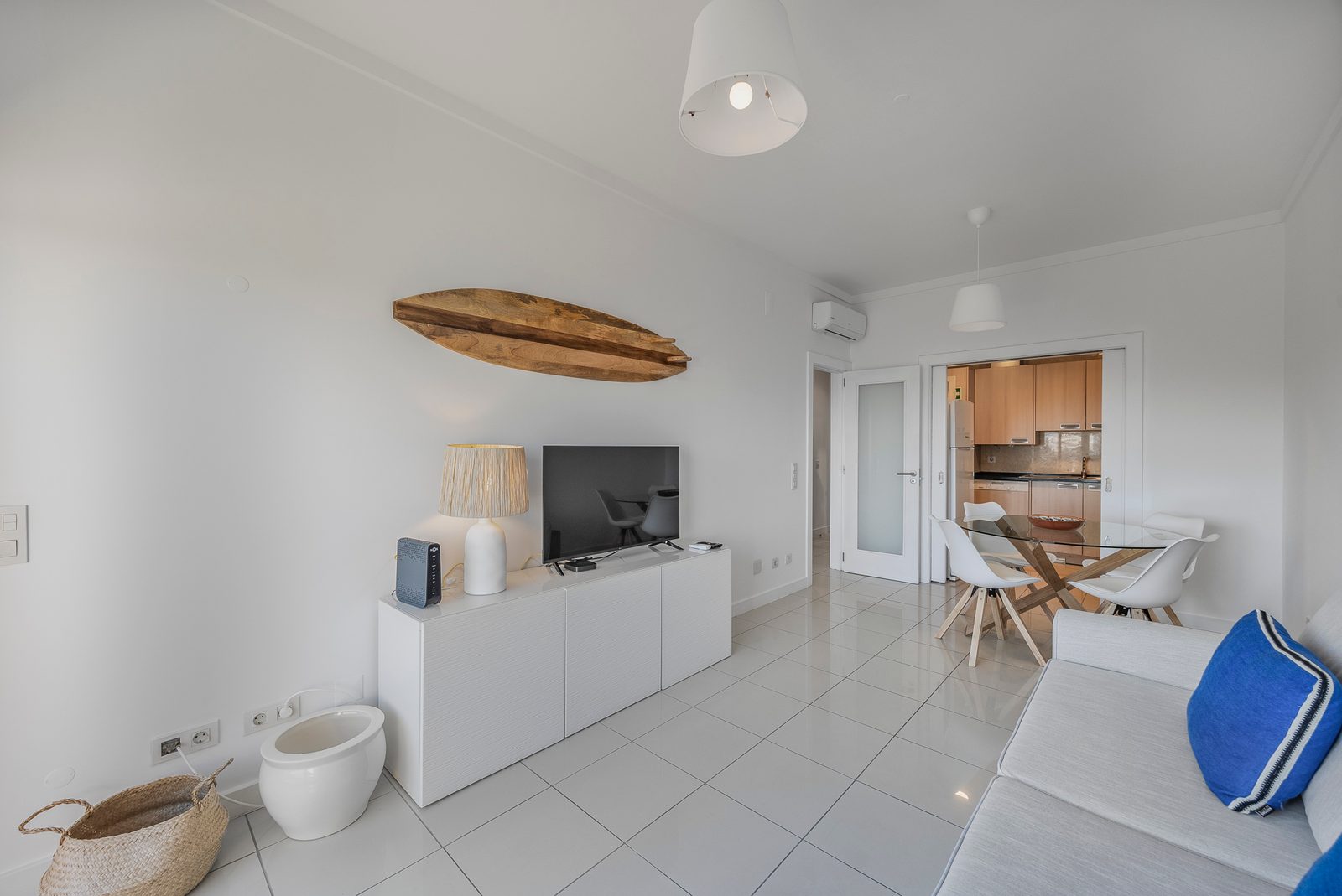 Living room with TV and surfboard decor, and the kitchen beyond