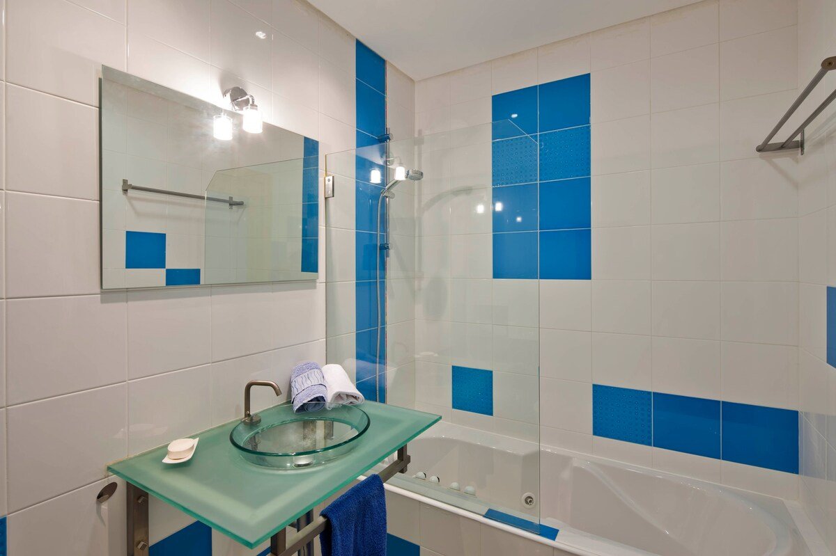 Bathroom with corner bathtub, glass shower screen, and blue mosaic tiling