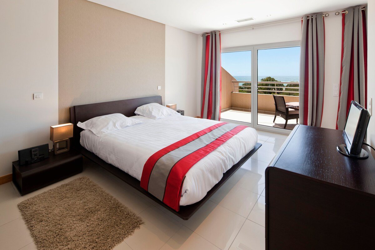 Bedroom with striped curtains, balcony access, and sea and tree views