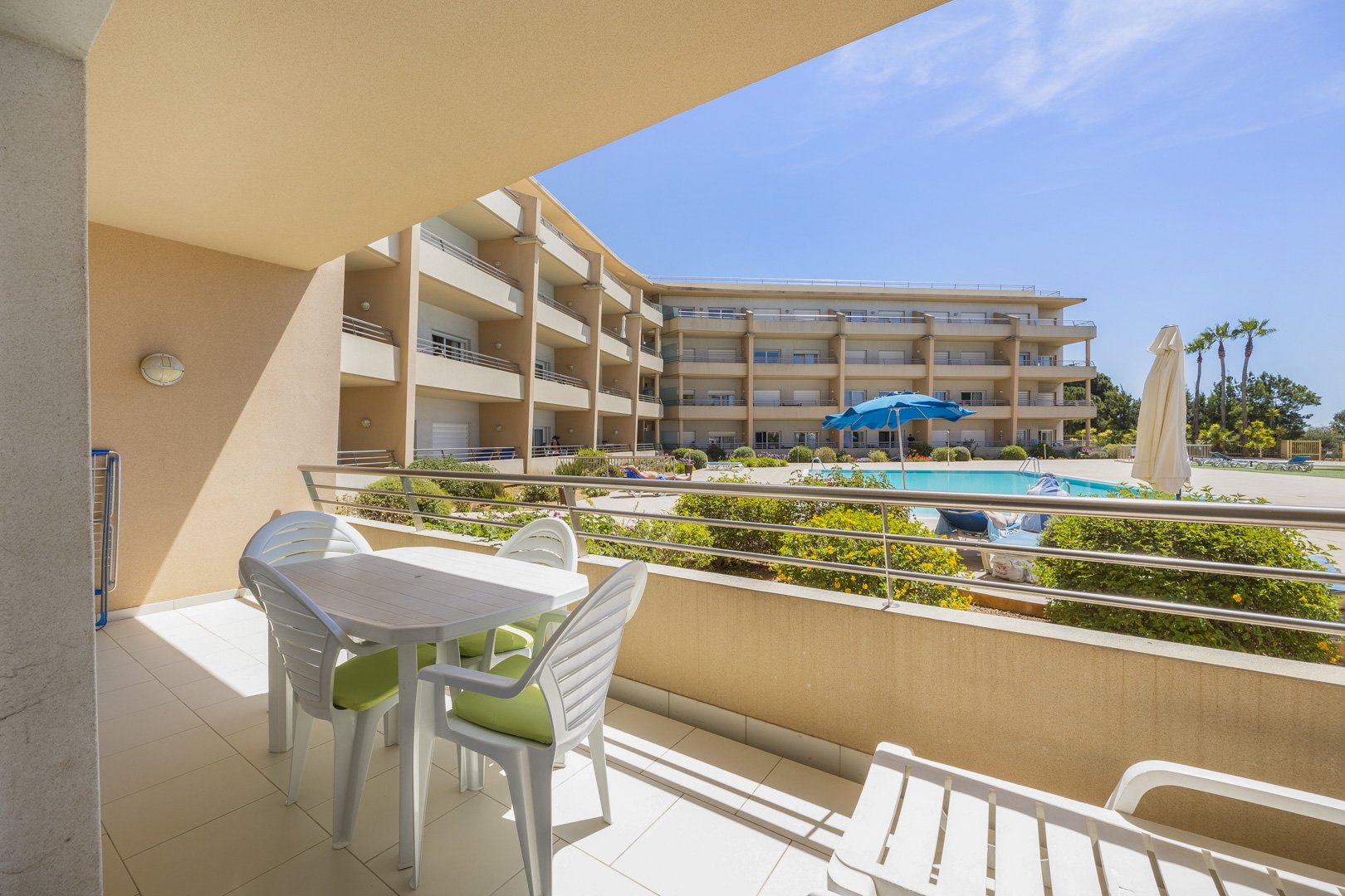 Balcony with dining table, sun lounger, and view over the pool and building