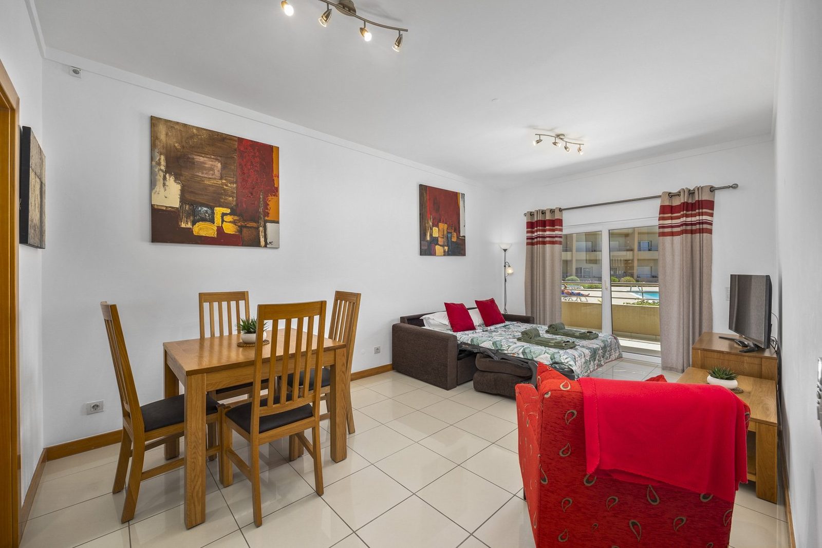 Living and dining area with sofa bed, dining table, and pool-view balcony access