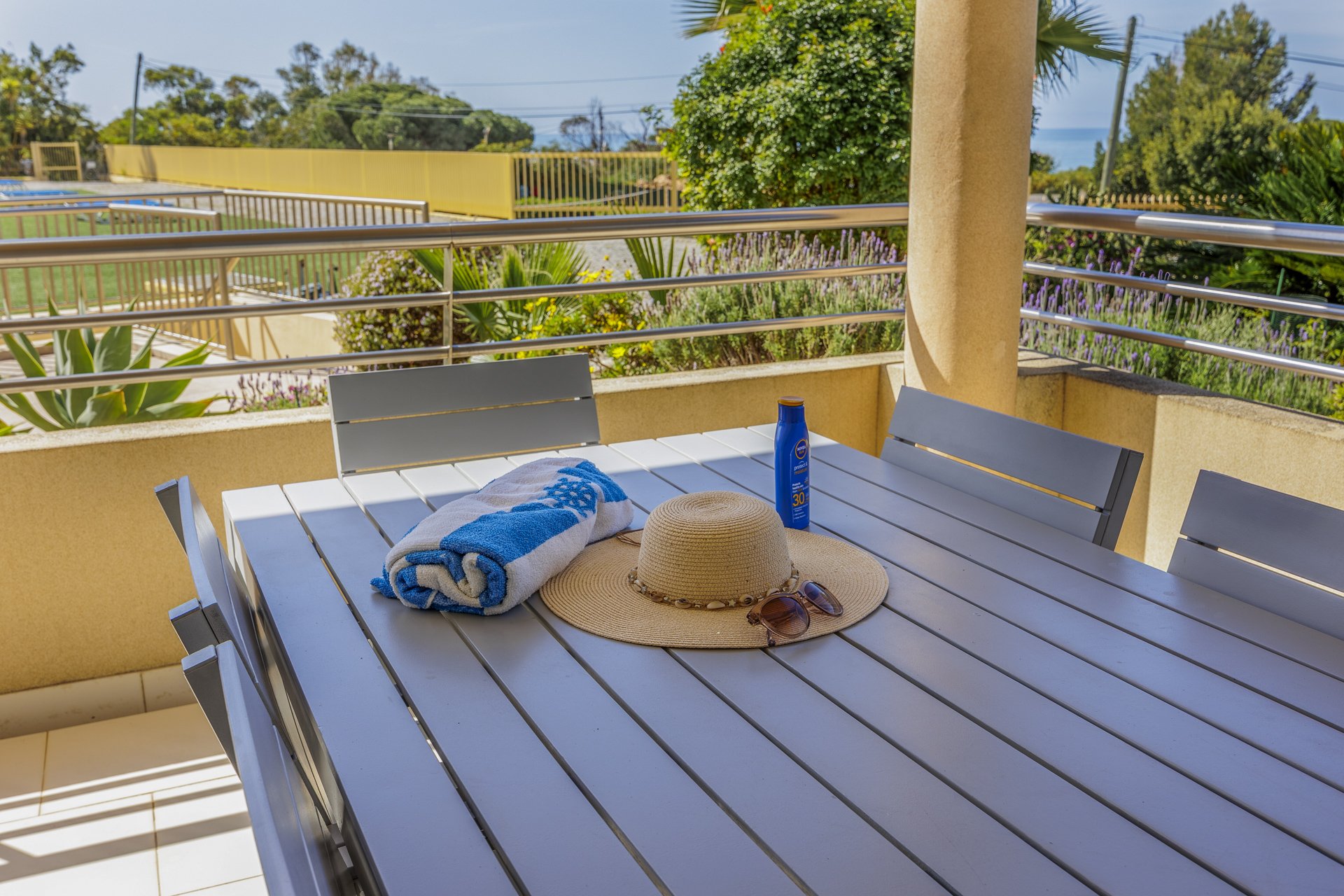 Balcony table set with beach towel, sun hat, and sunscreen