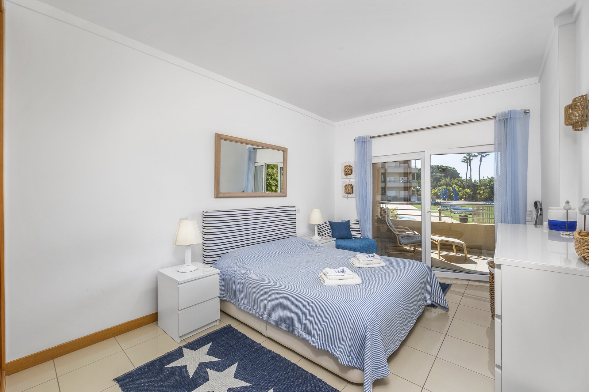Bedroom with striped headboard, mirror, and pool-view balcony access