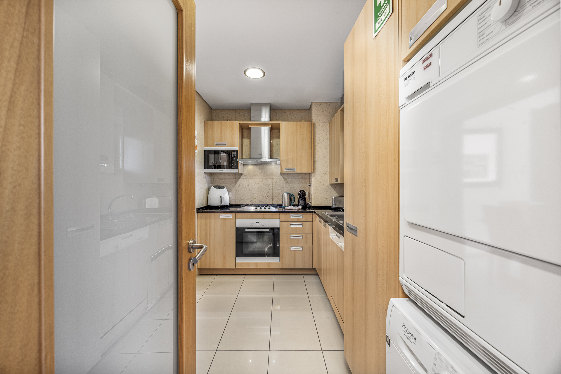 Kitchen viewed through the entrance hallway, with wooden cabinetry and a stacked washer-dryer