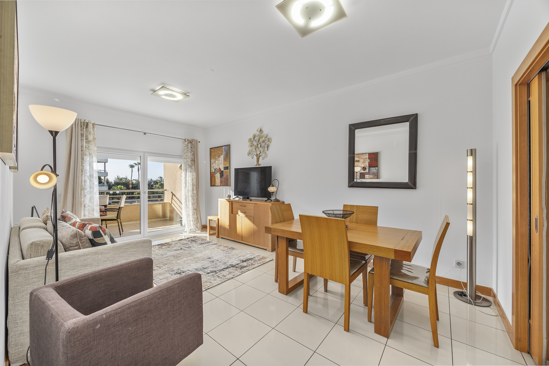 Living and dining area with armchair, sofa, and dining table opening onto the balcony