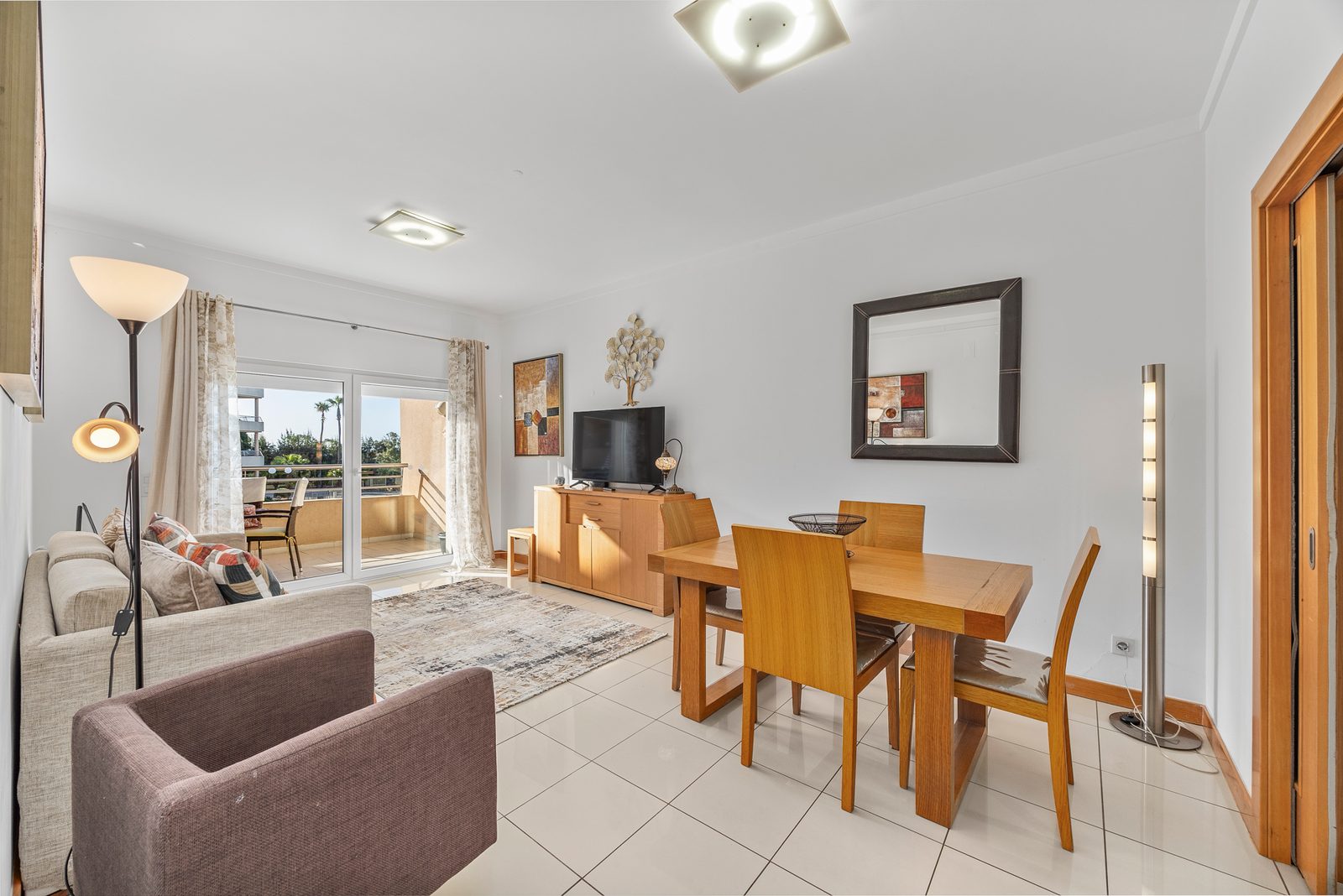 Living and dining area with armchair, sofa, and dining table opening onto the balcony