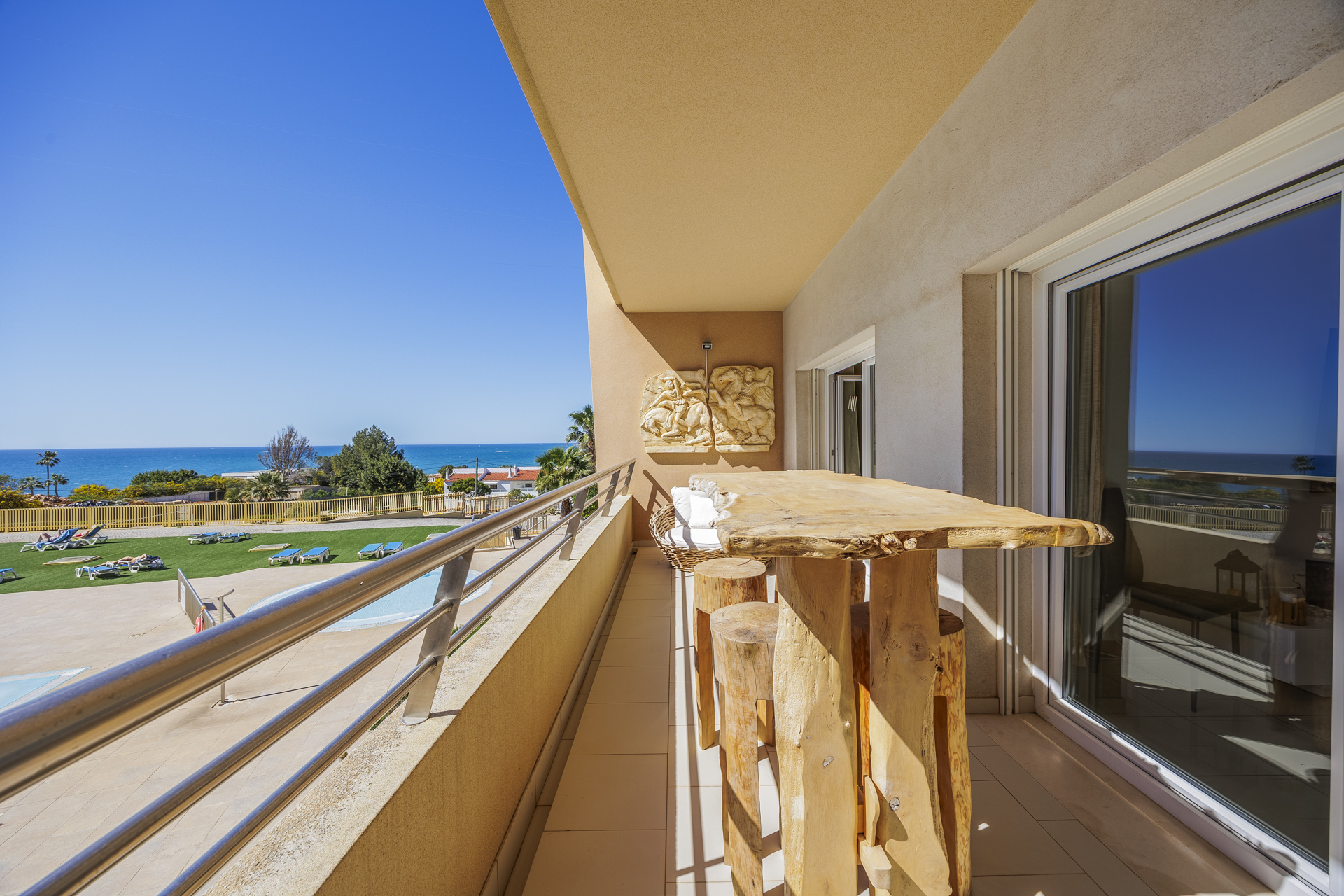 Balcony with a live-edge wooden table and sea view over the pool and gardens