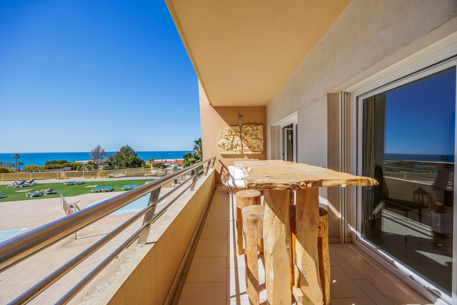 Balcony with a live-edge wooden table and sea view over the pool and gardens
