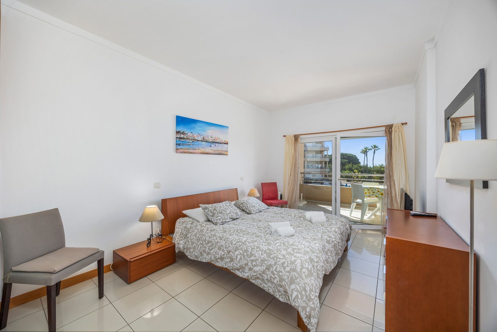 Bedroom with sea-view artwork, red armchair, and balcony access