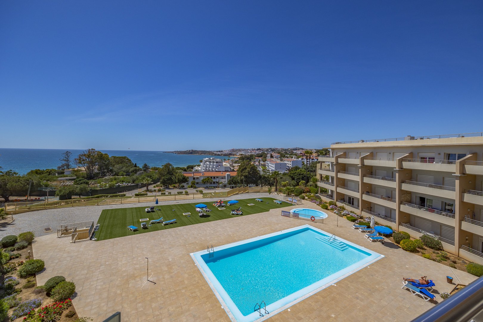 Elevated view of the communal pool, sun lawn, and the harbor and coastline