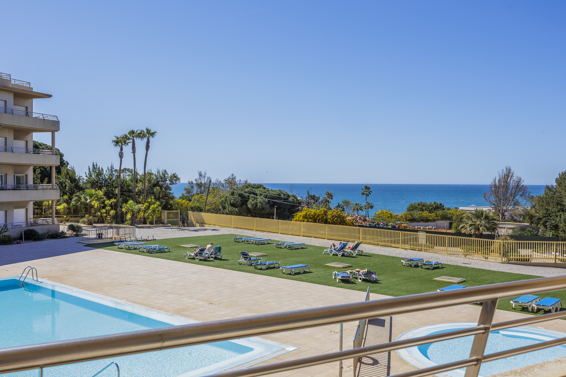 View over the pool and sun-lounger lawn toward the coastline