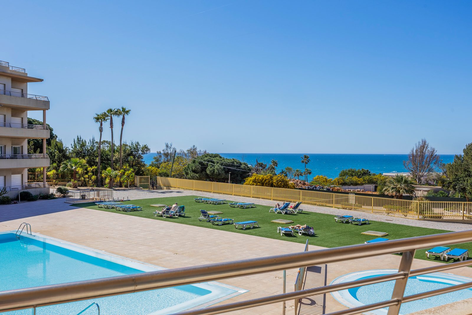 View over the pool and sun-lounger lawn toward the coastline