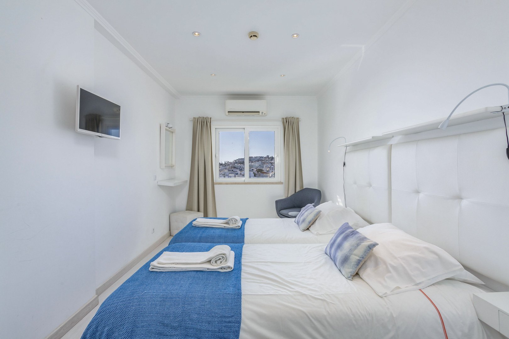 Twin bedroom with blue bedspreads, TV, and town view