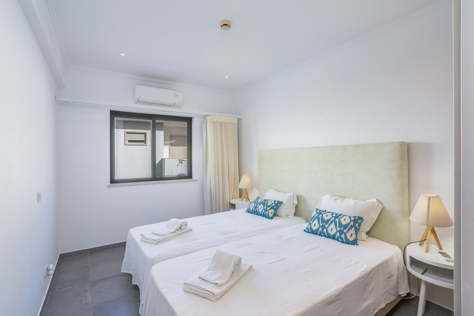 Twin bedroom with sage green headboard and balcony-view window