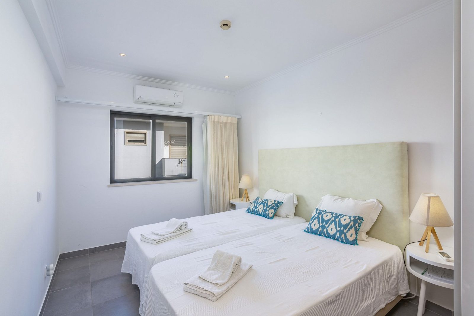 Twin bedroom with sage green headboard and balcony-view window